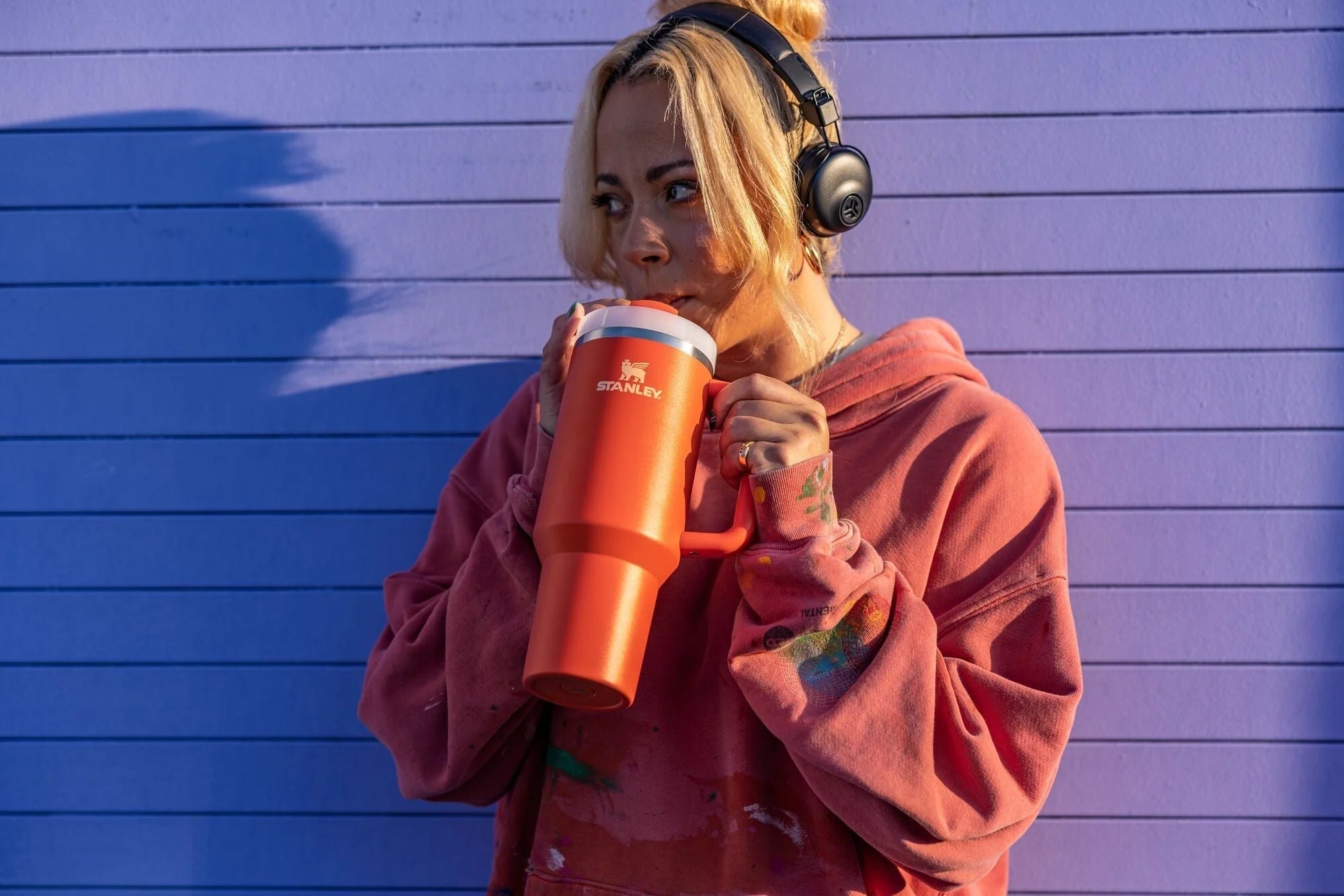 Person holding a tumbler against wearing headphones